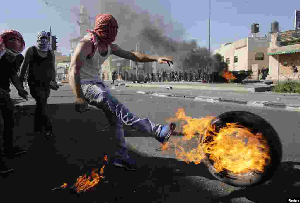 A Palestinian kicks a tire after setting it ablaze during clashes with Israeli police in Shuafat, an Arab suburb of Jerusalem. The discovery of a body in a Jerusalem forest raised suspicions that a missing Palestinian youth had been killed by Israelis avenging the deaths of three abducted Jewish teens.