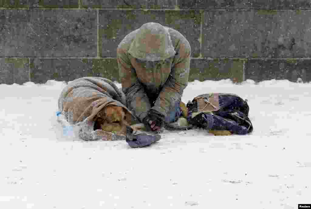 A man with his dog begs for money on the medieval Charles bridge during snowfall in Prague, Czech Republic.