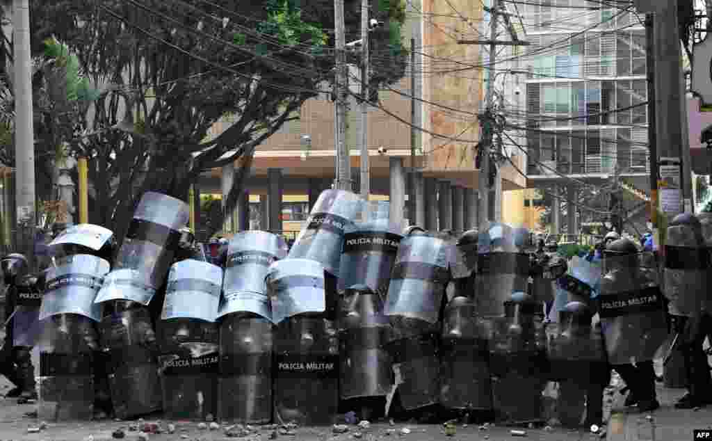 Honduran riot police take cover during clashes with students of the National Autonomous University of Honduras (UNAH) and elementary school teachers protesting against the approval of education and healthcare bills in the Honduran Congress in Tegucigalpa, April 29, 2019.