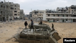 Warga Palestina mengamati tank militer Israel yang rusak dan ditinggalkan di wilayah Rafah di selatan Jalur Gaza, pada 22 Januari 2025. (Foto: Reuters/Hatem Khaled)