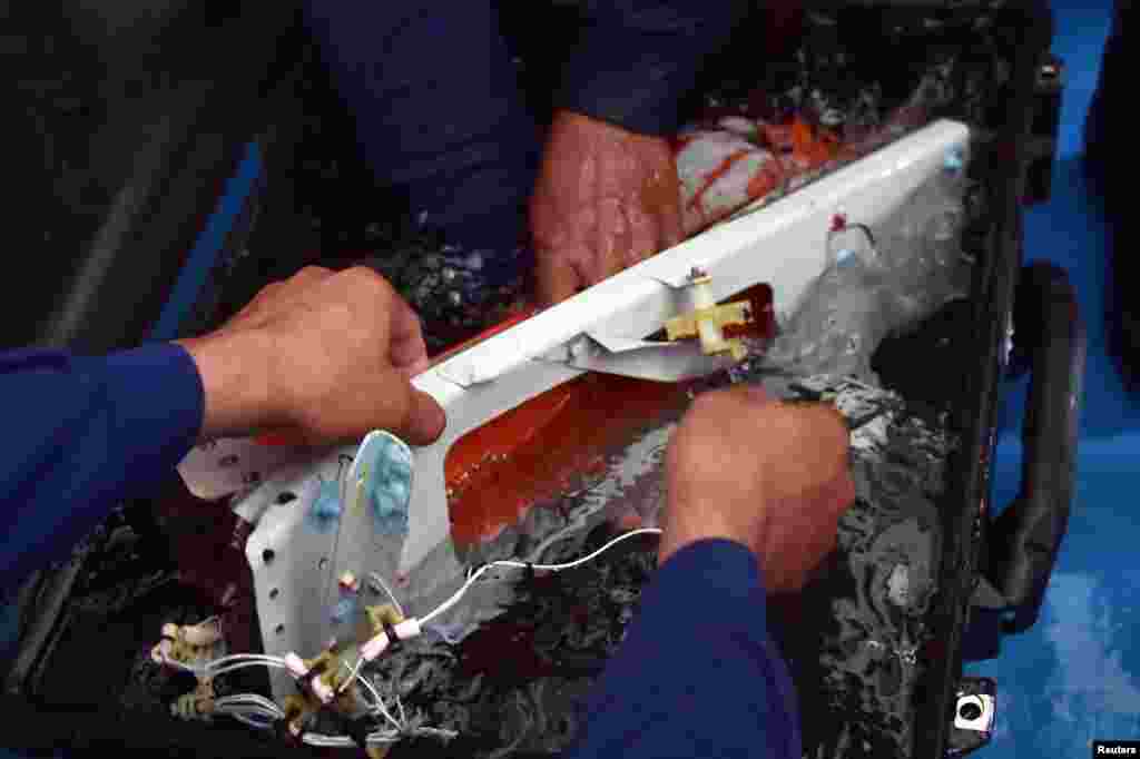 Indonesian divers hold the flight data recorder of AirAsia QZ8501 onboard the navy vessel KRI Banda Aceh, in the Java Sea, Jan. 12, 2015.