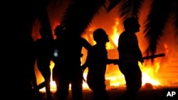 FILE - Libyan civilians watch fires at an Ansar al-Shariah Brigades compound, after hundreds of Libyans, Libyan Military, and Police raided the Brigades base, in Benghazi, Libya, Sept. 21, 2012.