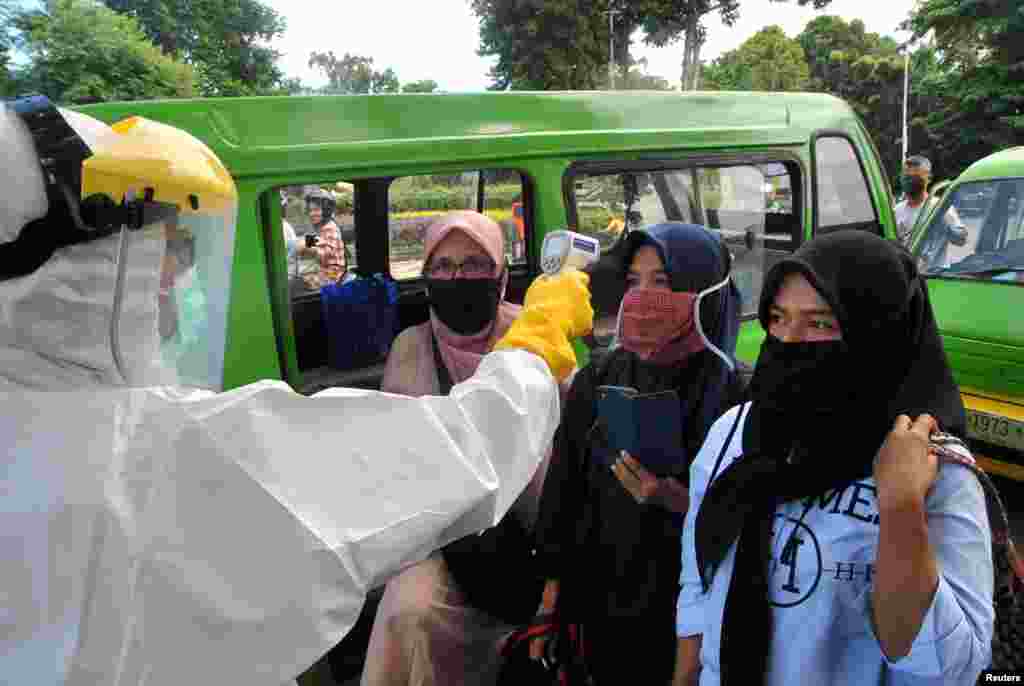 Un trabajador de la salud revisa la temperatura de los pasajeros con máscaras faciales en medio de la propagación del brote de la enfermedad por coronavirus (COVID-19), en una intersección de la carretera en Bogor, provincia de Java Occidental, Indonesia.