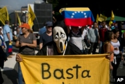 FILE - A protester, wearing a mask and holding a banner that reads in Spanish, "Stop," takes part in a protest against President Nicolas Maduro, in Caracas, Venezuela, Oct. 26, 2016.