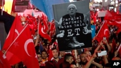 ພວກສະໜັບສະໜຸນຍ ປ. ເທີກີ ທ່ານ Recep Tayyip Erdogan ໂບກທຸງຊາດ ແລະຍົກຮູບ ນັກສອນສາສະໜາ Fethullah Gulen ທີ່ລີ້ໄພຢູ່ສະຫະລັດ ທີ່ທາງການເທີກີ ຕ້ອງການໂຕ. 