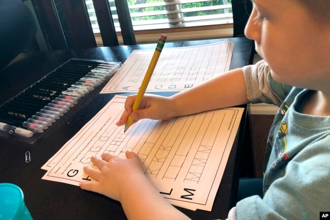 In this March 24, 2020, photo provided by Christina Rothermel-Branham, her son James, does school work at their Tahlequah, Okla. home.