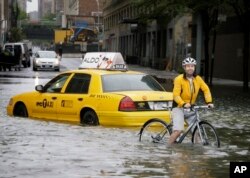 FILE - A bicyclist makes his way past a stranded taxi on a flooded New York City street as Tropical Storm Irene passes through the city, Aug. 28, 2011. A June 2012 study in Nature Climate Change said scientists and computer models were estimating that by the year 2100, sea levels globally could rise as much as 3.3 feet.
