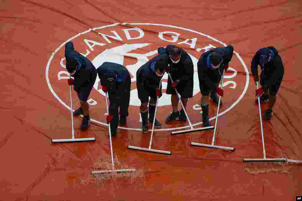 گروهی از کارگران در حال خالی کردن آب زمین تنیس در حاشیه مسابقات اوپن فرانسه. 