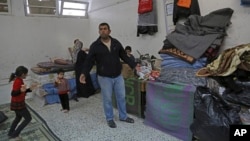 Sufian Wadiya, 36, whose home was destroyed by Israeli strikes during last summer's Israel-Hamas war, stands in front of his 12-member family's belongings at a U.N. school in Gaza City where they now live, Jan. 27, 2015. 