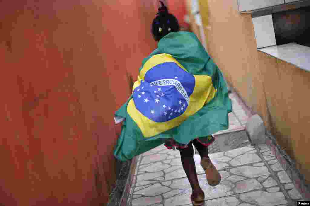 Seorang anak perempuan mengenakan bendera Brazil berlari di daerah kumuh Varjao di luar Brasilia, sebelum pertandingan grup A Piala Dunia 2014 antara Brazil dan Meksiko, 17 Juni 2014.