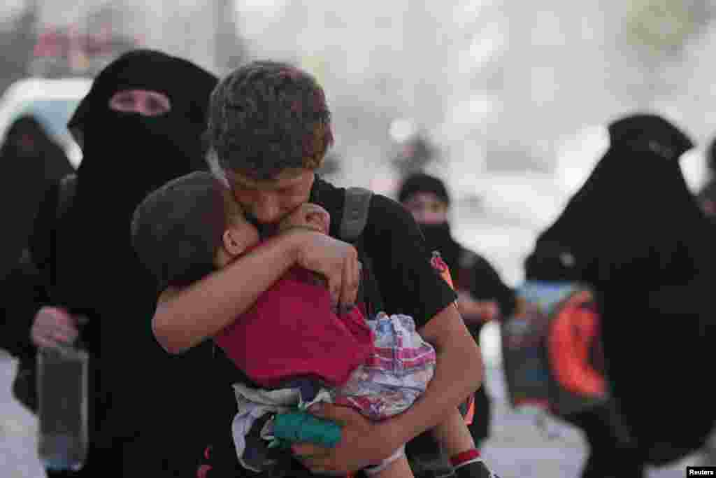 Seorang warga sipil menggendong anaknya saat berjalan bersama yang lainnya setelah dievakuasi oleh Pasukan Demokratis Suriah (SDF) dari kota Manbij yang dikuasai ISIS di Aleppo, Suriah (12/8). (Reuters/Rodi Said)
