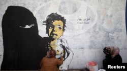 FILE - A friend of artist Haifa Subay takes pictures of her painting a mural she says represents the children and women suffering in Yemen's war, in Sanaa, Yemen, Feb. 21, 2019.