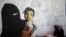 FILE - A friend of artist Haifa Subay takes pictures of her painting a mural she says represents the children and women suffering in Yemen's war, in Sanaa, Yemen, Feb. 21, 2019.