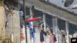 ARCHIVO - Reclusos señalan desde el interior de la cárcel La Modelo en Bogotá, Colombia, domingo 22 de marzo de 2020.
