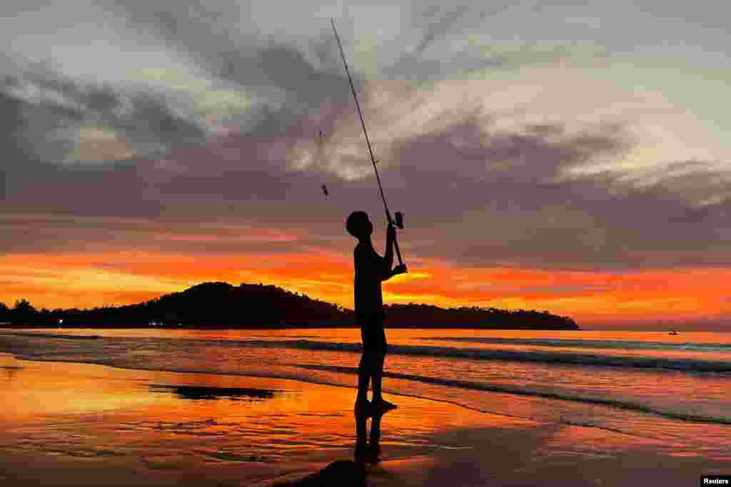 A boy fishes during sunset at Bang Tao beach in Phuket, Thailand, Dec. 6, 2021.