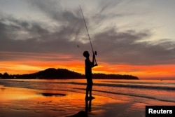 Seorang anak laki-laki memancing saat matahari terbenam di Pantai Bang Tao di Phuket, Thailand, 6 Desember 2021. (Foto: Reuters)