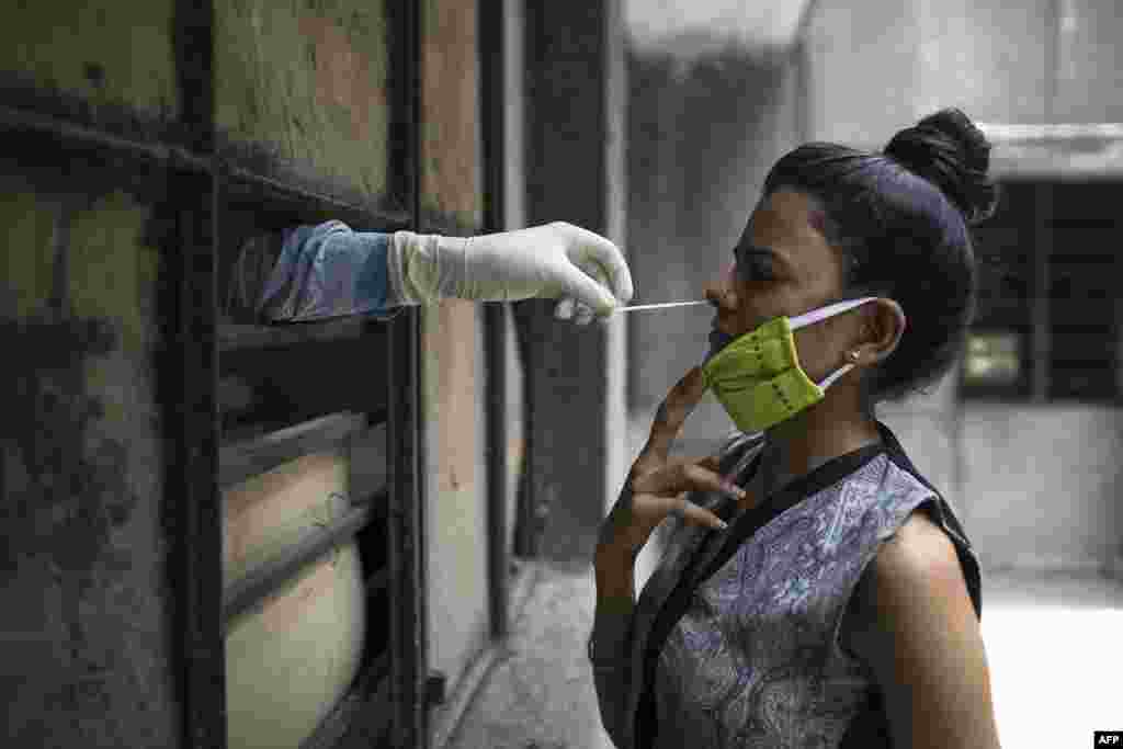 A health official, left, administers a coronavirus test to a woman at a temporary, free testing center set up in a school after officials eased lockdown restrictions, in New Delhi, India.