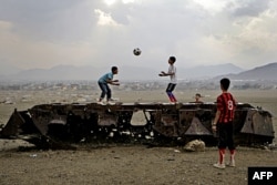 FILE - Afghan boys play with a ball on top of the remains of a Russian armored vehicle in Kabul, Afghanistan, Oct. 6, 2011.