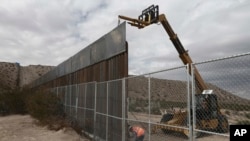 FILE - Workers raise a taller fence along the Mexico-US border between the towns of Anapra, Mexico and Sunland Park, New Mexico, Nov. 10, 2016. For almost two decades, a Mass has been celebrated there on the Day of the Dead to remember migrants who have 