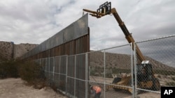 FILE - Workers raise a taller fence along the Mexico-U.S. border between the towns of Anapra, Mexico, and Sunland Park, New Mexico, Nov. 10, 2016.