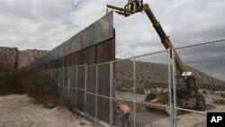  FILE - Workers raise a taller fence along the Mexico-US border between the towns of Anapra, Mexico and Sunland Park, New Mexico, Nov. 10, 2016. 