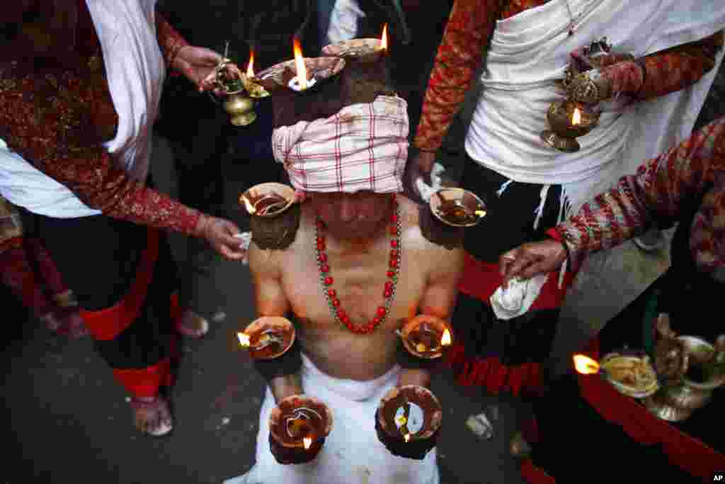 Seorang Hindu dari Nepal mengatur keseimbangan lampu yang menyala di sepanjang lengannya dalam Festival Madhav Narayan di Lalitpur, di pinggiran Kathmandu, Nepal.