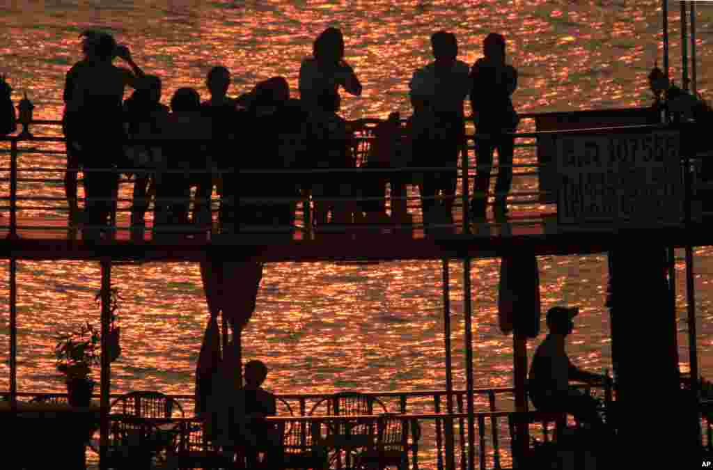 Bóng của các du khách in trên nền trời khi ngắm mặt trời lặn từ mái của một con thuyền bằng gỗ trên sông Tonle Sap gần làng Chroy Changvar tại Phnom Penh. Campuchia. (AP) 