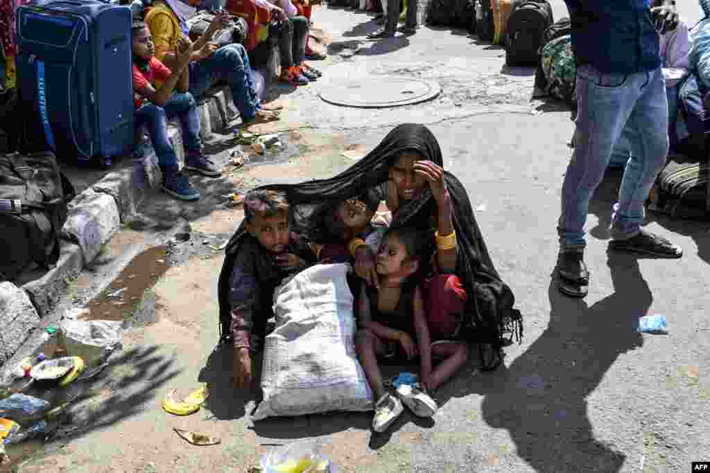 A woman covers her children with a shawl to protect them from the sun as she waits with other migrant workers and families for a train going to their home towns after the government eased a nationwide coronavirus lockdown in New Delhi, India.