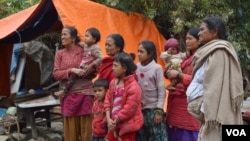 A family stands next to a tent in front of their destroyed home. They prefer to stay here instead of sheltering in a school because they are worried about their valuables being plundered from the rubble, Sankhu, Nepal, April 29, 2015. (Steve Herman/VOA)