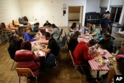 FILE - A group of homeless people, including Ellen Tara James-Penney (wearing blue) left, a lecturer at San Jose State University, receive a meal at Grace Baptist Church in San Jose, California, Oct. 10, 2017.