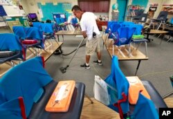 Custodian Jaime Cordona vacuums an empty second-grade classroom at San Marcos Elementary School, April 26, 2018, in Chandler, Ariz. Teachers in Arizona and Colorado walked out over low salaries, keeping hundreds of thousands of students out of school.