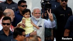 India's Prime Minister Narendra Modi holds the granddaughter of India's ruling Bharatiya Janata Party (BJP) president Amit Shah after he arrives to cast his vote at a polling station in Ahmedabad, April 23, 2019.