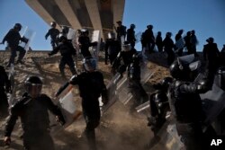 Mexican police run as they try to keep migrants from getting past the Chaparral border crossing in Tijuana, Mexico, Sunday, Nov. 25, 2018, near San Ysidro, California.