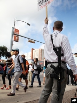 Andrew Clements, right, a licensed gun owner, open carrying a high-velocity rifle, demonstrates on Guadalupe St., next to the University of Texas, in Austin, Texas, Aug. 24, 2016.