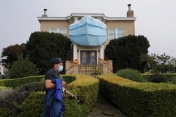 FILE - A man walks past a large face mask hanging over pumpkins in front of a house during the coronavirus pandemic in San Francisco.