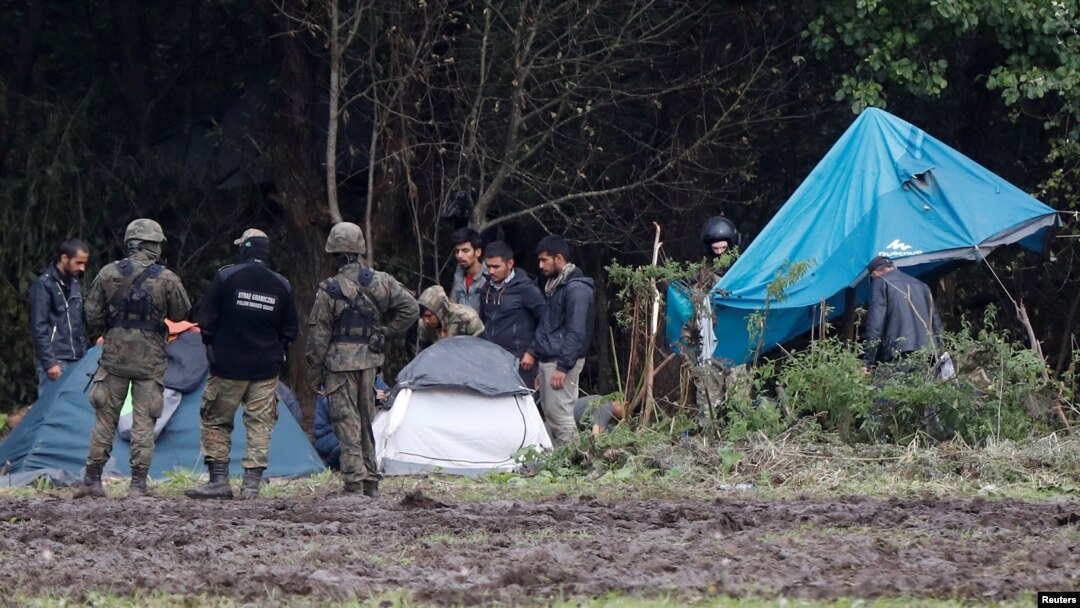 Petugas penjaga perbatasan wilayah Polandia tampak berdiri di dekat sekelompok migran yang terdampar di perbatasan antara Polandia dan Belarus di dekat desa Usnarz Gorny, Polandia, pada 1 September 2021. (Foto: Reuters/Kacper Pempel)