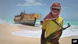 FILE — In this September 23, 2012 photo, masked Somali pirate Hassan stands near a Taiwanese fishing vessel that washed up on shore after the pirates were paid a ransom and released the crew, in the once-bustling pirate den of Hobyo, Somalia. 