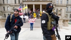 FILE - In this April 15, 2020, photo protesters carry rifles near the steps of the Michigan State Capitol in Lansing, Mich. 