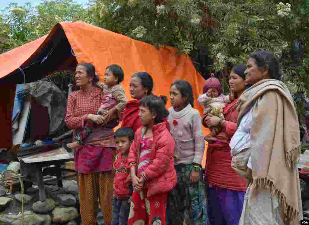 A family stands next to a tent in front of their destroyed home. They prefer to stay here instead of sheltering in a school because they are worried about their valuables being plundered from the rubble, Sankhu, Nepal, April 29, 2015. (Steve Herman/VOA)