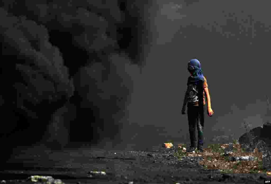 A Palestinian demonstrator watches as smoke billows from a fire during clashes with Israeli forces following a weekly protest against the expropriation of Palestinian land by Israel, in the village of Kfar Qaddum, in the Israeli-occupied West Bank.