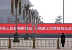 FILE - A paramilitary policeman stands guard in front of a screen displaying propaganda slogans on a deserted Tiananmen Square in Beijing, Nov. 15, 2012.