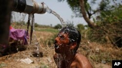 FILE - An Indian man takes bath under the tap of a water tanker on a hot day in Ahmadabad, India.