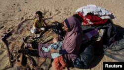 FILE - A woman sits with children outside, as displaced Palestinians, who fled their houses due to Israeli strike, shelter in a camp in Rafah, amid the ongoing conflict between Israel and Palestinian Islamist group Hamas, in the southern Gaza Strip, December 6, 2023