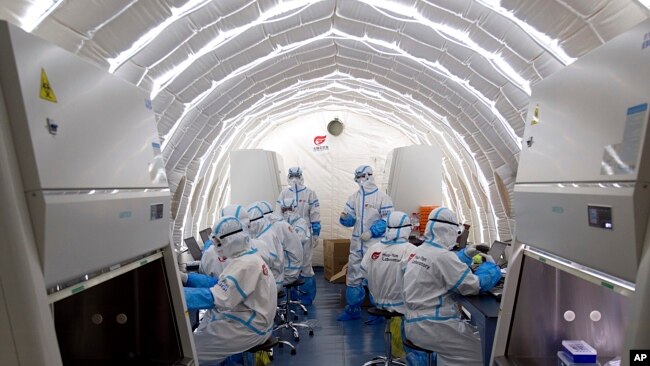 FILE - In this photo released by China's Xinhua News Agency, staff members work in an inflatable COVID-19 testing lab provided by Chinese biotech company BGI Genomics, a subsidiary of BGI Group, in Beijing, June 23, 2020.