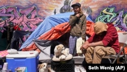 Lucio Lopez (kiri) berbincang dengan teman-temannya di depan tenda yang berada di kawasan tunawisma di Queens, New York, 13 April 2021. (Foto: Seth Wenig/AP)