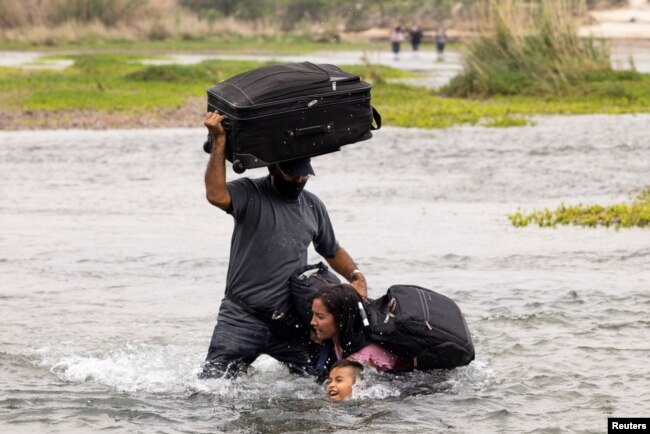 FILE - Asylum-seeking migrants cross the Rio Grande river into the United States from Mexico, in Del Rio, Texas, May 10, 2021.