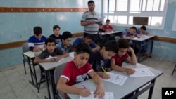 In this Sunday, May 26, 2019 photo, a teacher supervises while Palestinian school children attend a final exam during the last day of the school year, at the UNRWA, Hebron Boys School, in the West Bank city of Hebron. (AP Photo/Nasser Nasser)