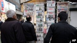 Iranians look at newspapers hanging on a news stand in central Tehran, Feb. 25, 2012.