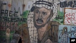 Woman passes near section of Israel's separation barrier depicting Yasser Arafat near the West Bank city of Ramallah, Aug. 8, 2012.