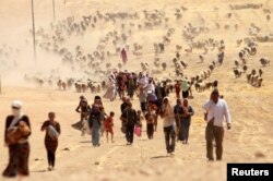 FILE - Displaced people from the minority Yazidi sect, fleeing violence from forces loyal to the Islamic State in Sinjar town, walk toward the Syrian border, on the outskirts of Sinjar mountain, near the Syrian border town of Elierbeh of Al-Hasakah governorate, Iraq, Aug. 10, 2014.